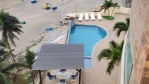 A beach view from a hotel balcony with a pool, lounge chairs, and palm trees. - On the Beach!  - walk to the mall and restaurants!  Great for remote workers (Manta)