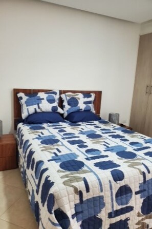 Une chambre à coucher comprenant un lit, une tête de lit en bois, deux tables de chevet et une armoire.