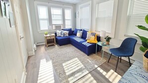 A modern living room with a blue sectional sofa, a small side table, a blue armchair, and a patterned rug.