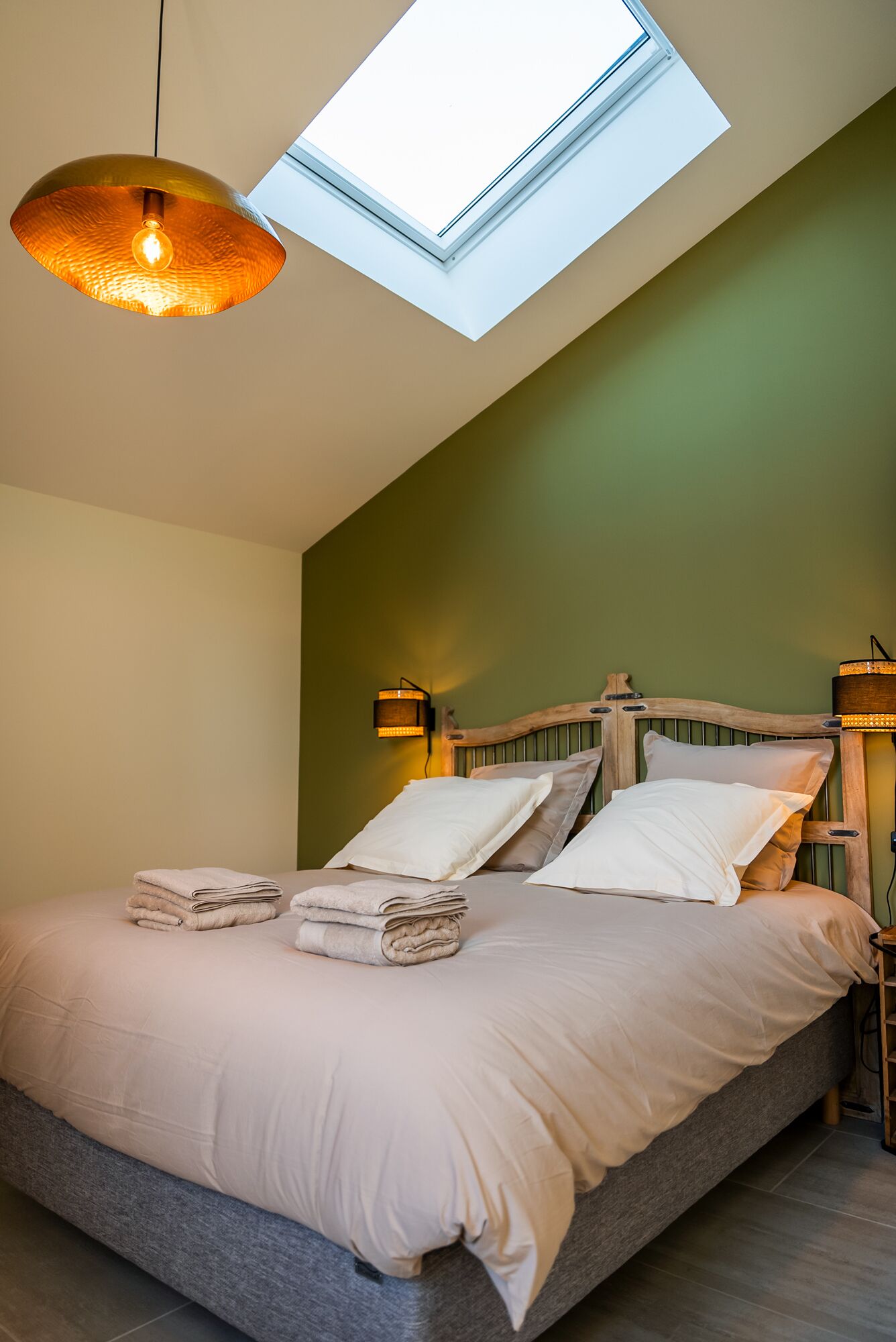Une chambre avec un puits de lumière, un lit avec des oreillers et une lampe fixée au mur.