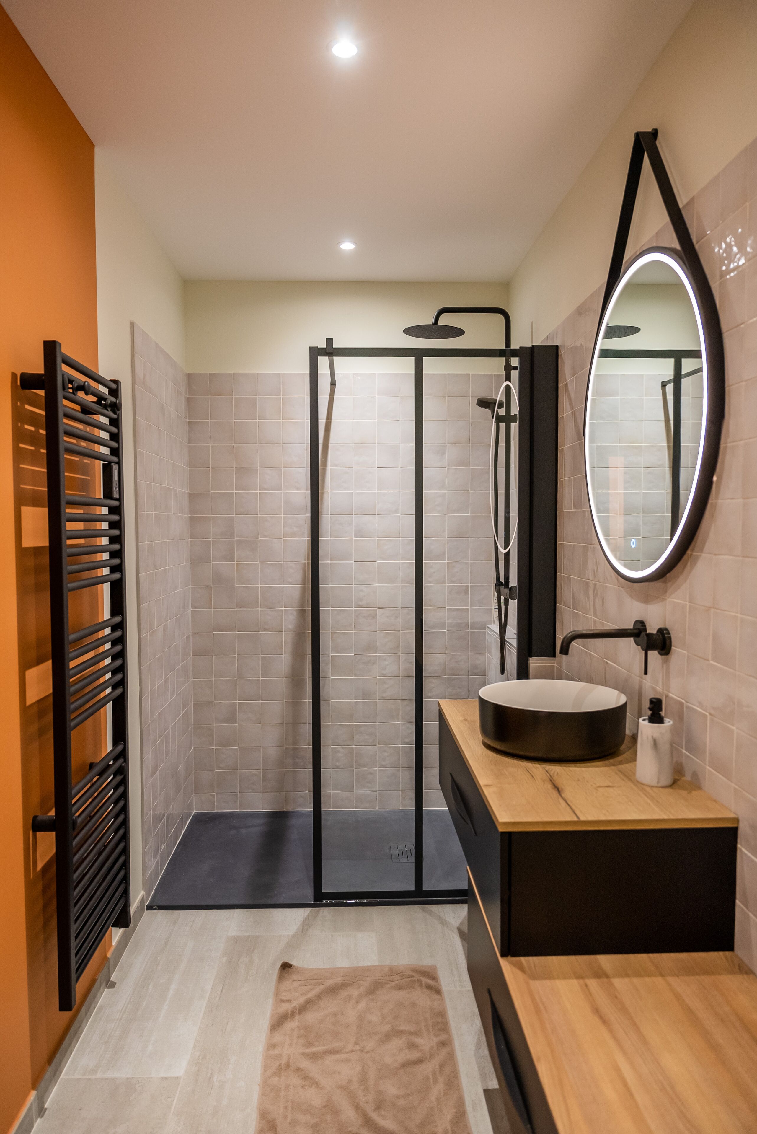 Un baño moderno con ducha acristalada, lavabo redondo y un espejo grande.