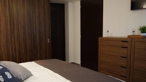 A bedroom with a bed, a wardrobe, a dresser, and a TV mounted on the wall.