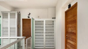 A hallway with a wooden door, a white door with horizontal blinds, and a glass railing.