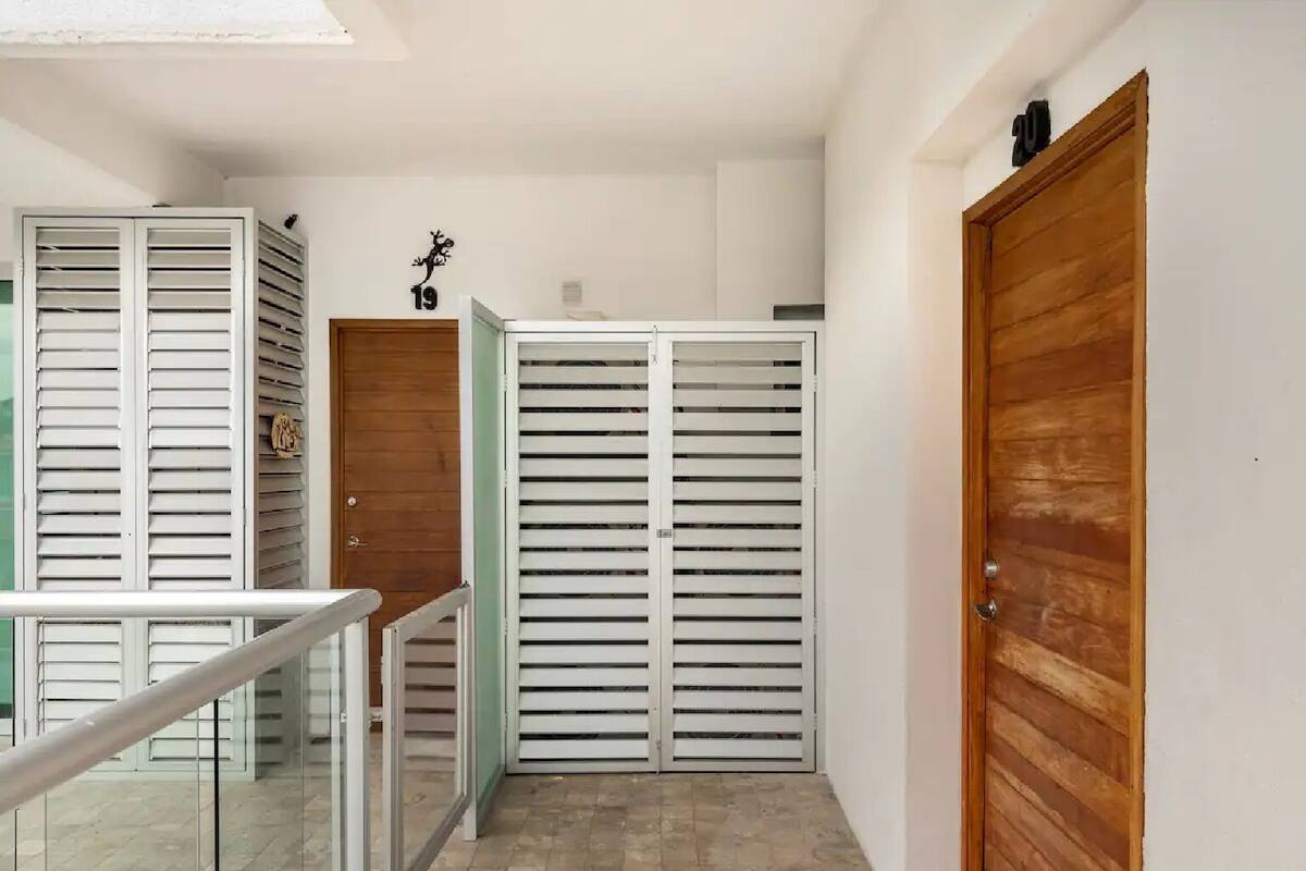 Un couloir avec une porte en bois, une porte blanche dotée de stores horizontaux et une rambarde en verre.