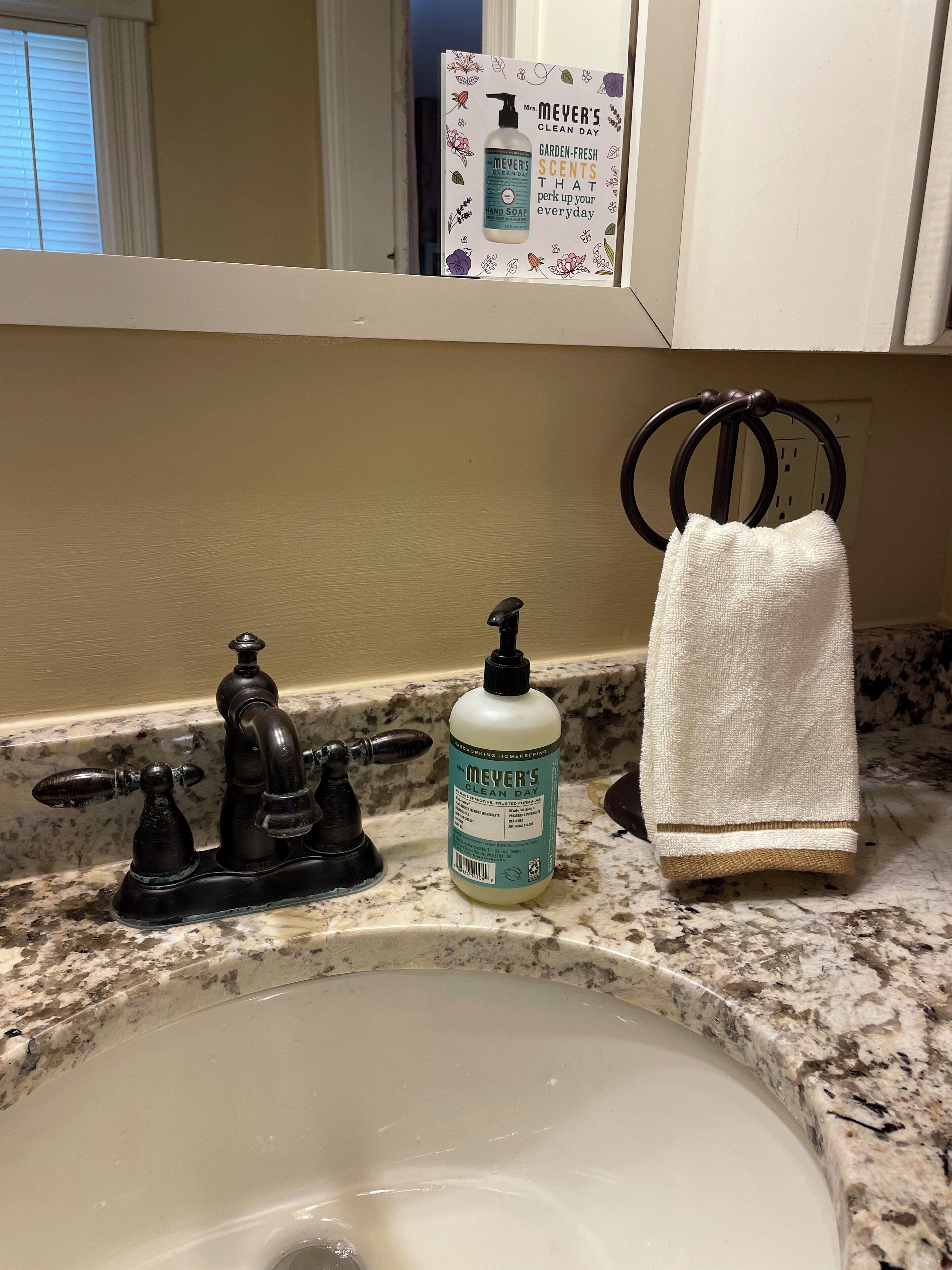 Un lavabo de salle de bain avec un robinet d’époque, un flacon de savon liquide pour les mains de la marque Meyer’s Clean Day et une serviette blanche suspendue à un porte-serviettes.