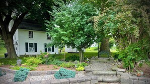 A stone staircase leading up to a wooden deck surrounded by a garden with various plants and a white house in the background. - Relax at The Farmhouse at Kindred Ground (Avon)