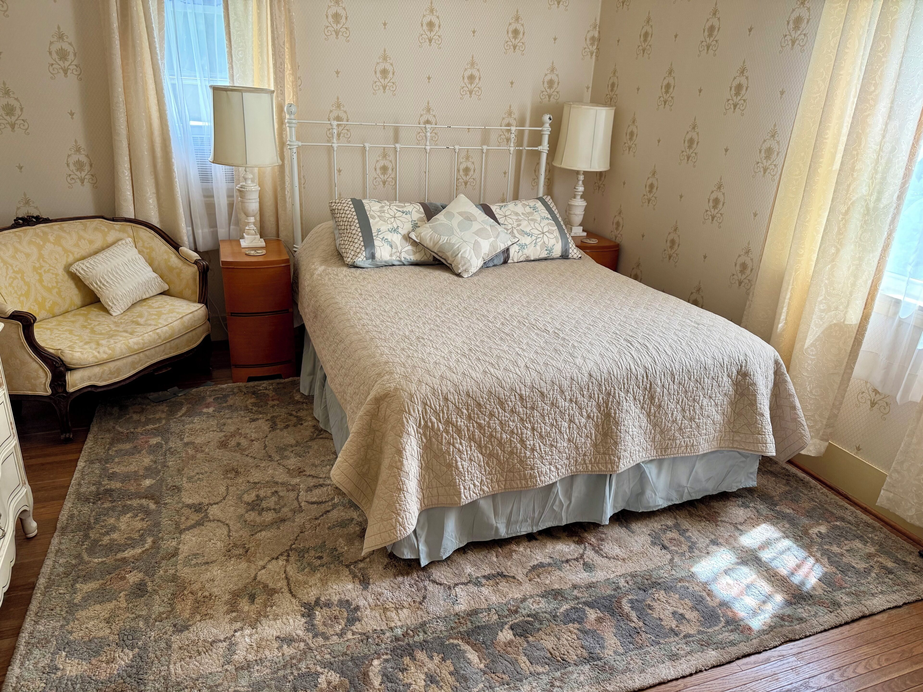 A bedroom with a bed, a chair, a nightstand, and a patterned rug.