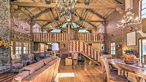 A spacious log cabin interior with a wooden staircase, leather seating, and a dining area with a centerpiece. - Countryside Cabin Retreat w/ Outdoor Kitchen! (Rienzi)