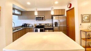 Une cuisine moderne dotée d’appareils électroménagers en acier inoxydable, d’un îlot central et de luminaires suspendus.