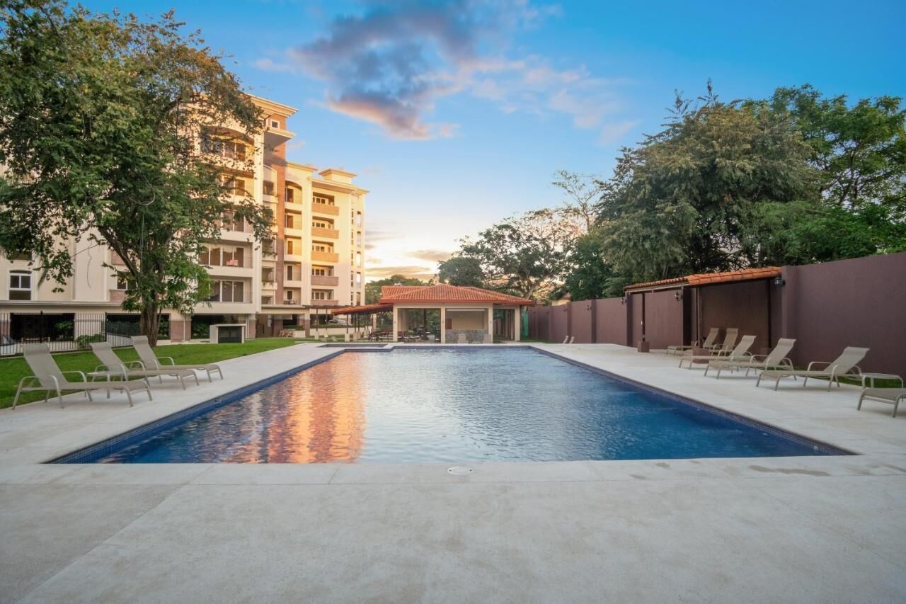 A swimming pool with lounge chairs, surrounded by buildings and trees.