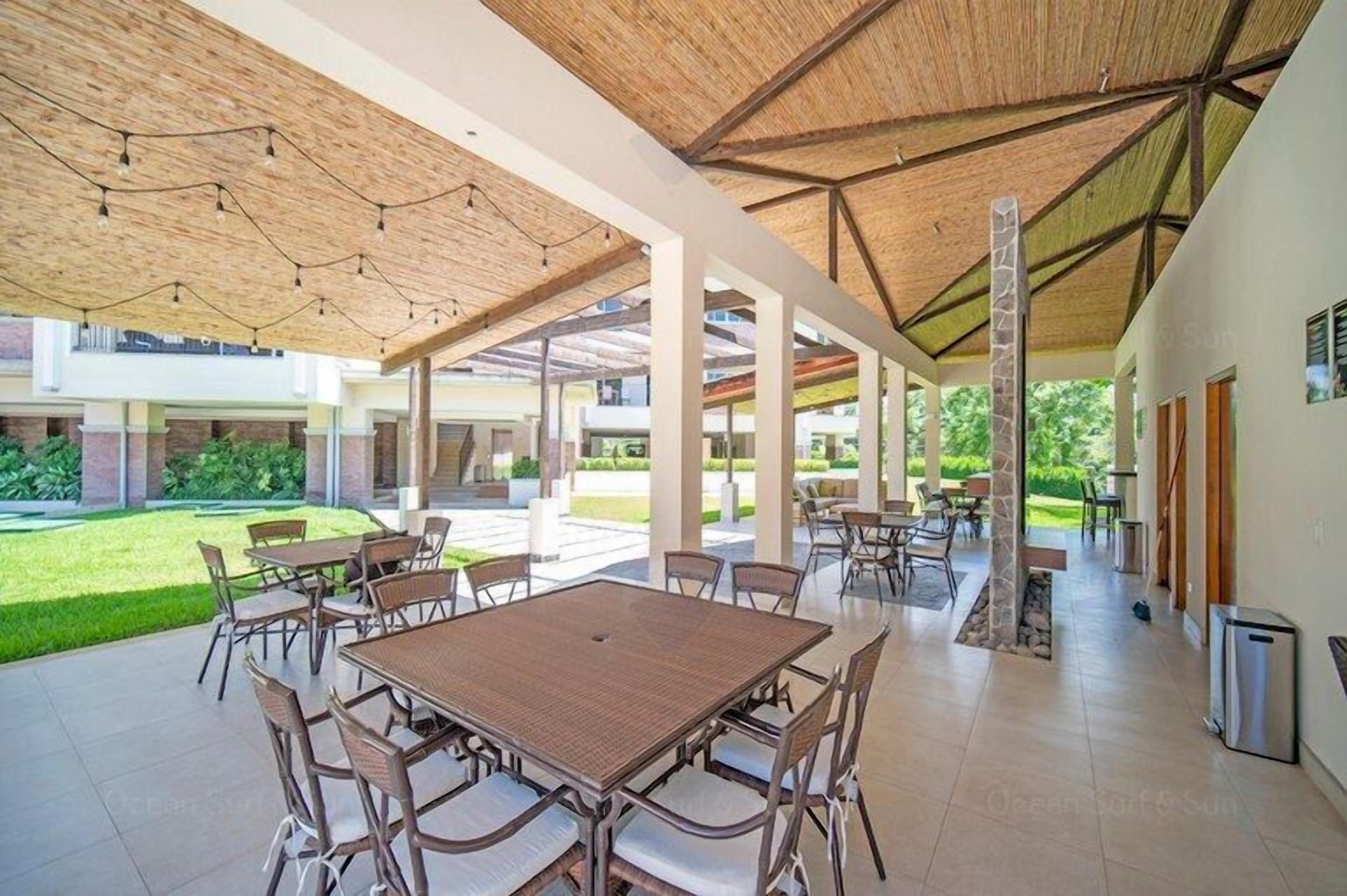 An outdoor covered patio with tables and chairs, a stone pillar, and a view of the surrounding greenery.