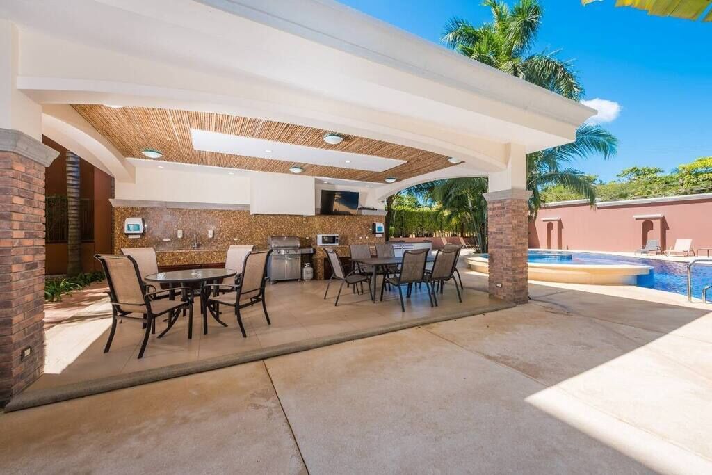 Un patio exterior con zona de barbacoa, piscina y zona de estar cubierta.