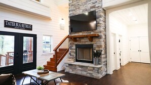 A spacious living area with a stone fireplace, a mounted TV, and a sign reading "TATER BUG RETREAT EST. 2021". - Stunning Farmhouse 1 mile to new casino sleeps 10 Hot Tub (Broken Bow)