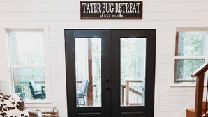 A living room with a leather sofa, a coffee table with a rustic centerpiece, and a large cowhide rug. A sign above the door reads "TATER BUG RETREAT EST. 2021". - Stunning Farmhouse 1 mile to new casino sleeps 10 Hot Tub (Broken Bow)