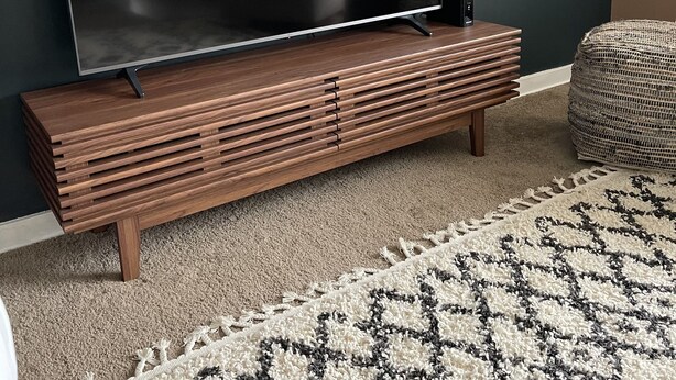 A flat-screen TV on a wooden TV stand in a living room with a patterned rug.