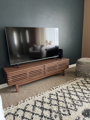 A flat-screen TV on a wooden TV stand in a living room with a patterned rug. - Cozy Home in Ironwood, MI (Ironwood)