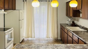 A kitchen with wooden cabinets, a white refrigerator, a built-in oven, a granite countertop, a sink, and three pendant lights.