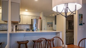 A modern kitchen with a central island, stainless steel appliances, and wooden chairs around a dining table.