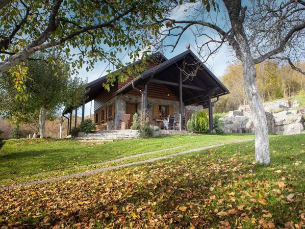 Relax on the covered porch with outdoor seating, surrounded by a serene natural landscape and well-maintained lawn.