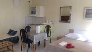 A small, well-lit room with a bed, a desk with a chair, a sofa, and a small kitchenette. - Apartments Bay View - Studio with Balcony (Podstrana)