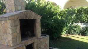 An outdoor stone-built pizza oven with a chimney, surrounded by a well-maintained garden and a building in the background. - Apartments Bay View - Studio with Balcony (Podstrana)