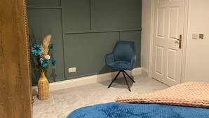 A room with a green accent wall, a blue chair, a wicker vase with flowers, and a bed with a blue blanket. - Log Cabin in Beautiful Countryside and Very Private (market rasen)