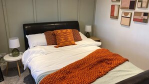 A neatly made bed with white linens and orange accents, a black headboard, and a wall with abstract art. - Log Cabin in Beautiful Countryside and Very Private (market rasen)