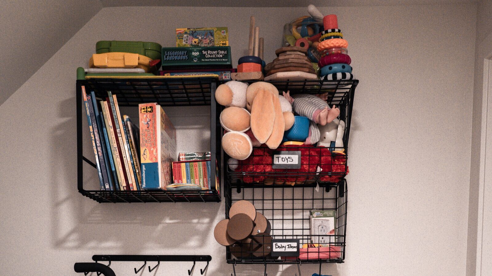 A storage area with two black wire baskets labeled "TOYS" and "Baby Clothes." One basket contains books, and the other holds various baby items and toys.