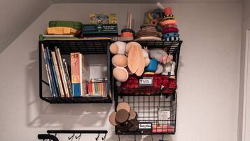 A storage area with two black wire baskets labeled "TOYS" and "Baby Clothes." One basket contains books, and the other holds various baby items and toys.