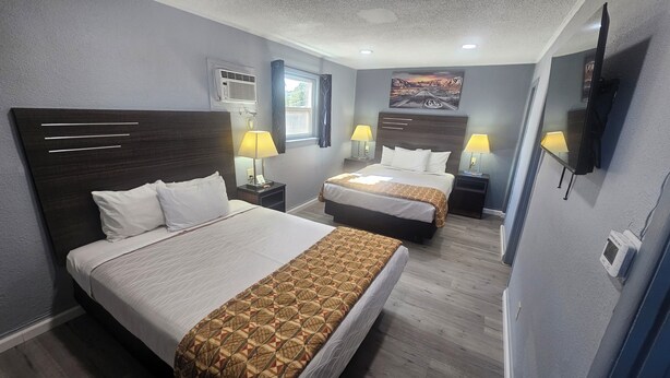 Une chambre d’hôtel avec deux lits, un téléviseur, une fenêtre avec des rideaux, un appareil de climatisation et un tableau au mur.