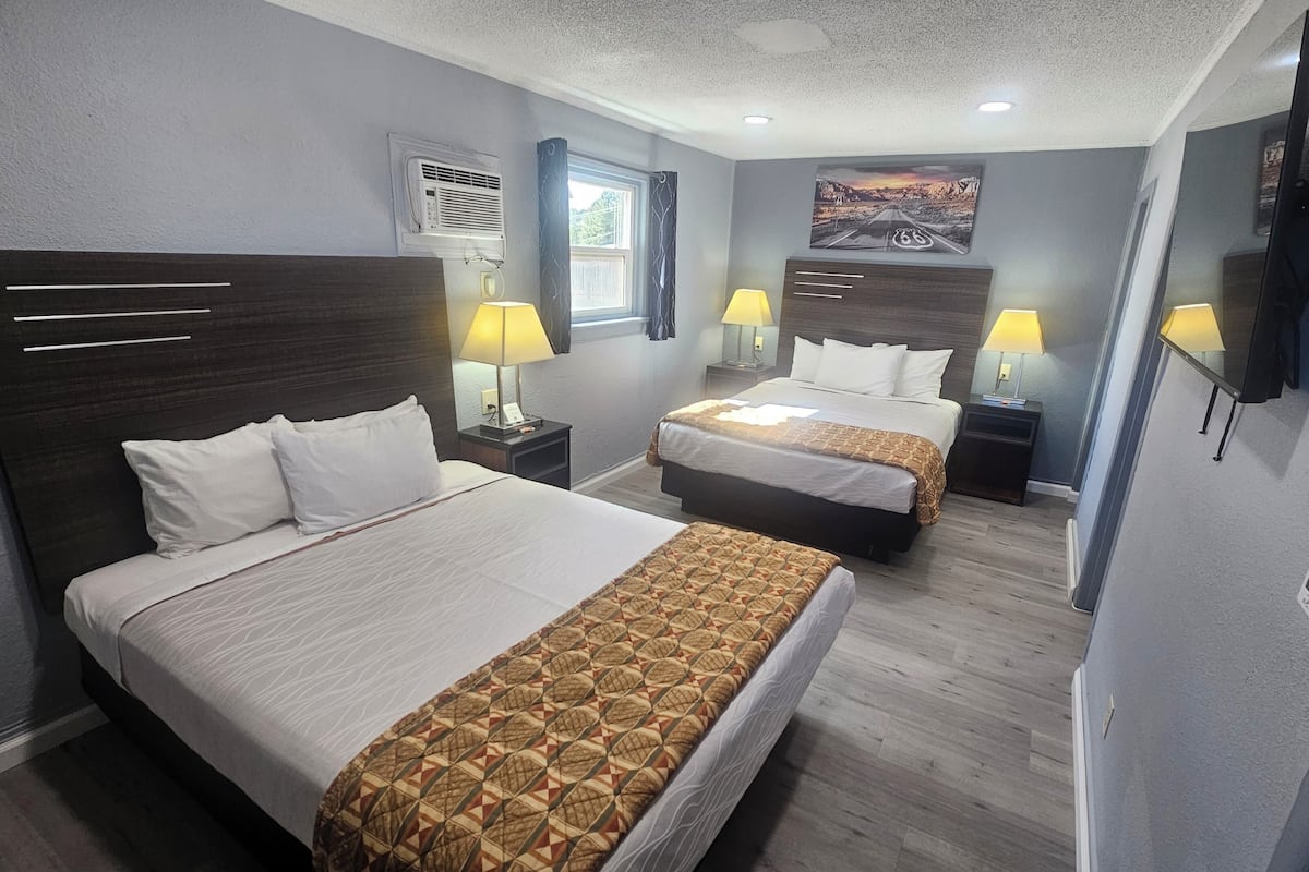 Une chambre d’hôtel avec deux lits, un téléviseur, une fenêtre avec des rideaux, un appareil de climatisation et un tableau au mur.
