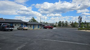 Un estacionamiento con varios vehículos, incluyendo una camioneta pickup y un sedán, frente a un edificio con una puerta azul y un letrero que dice Travelers Inn.
