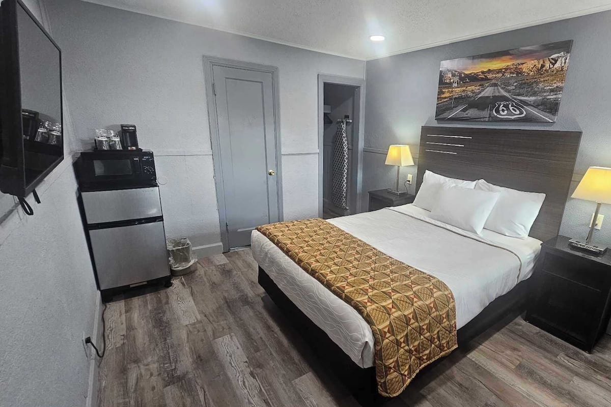Une chambre d’hôtel comprenant un lit, deux tables de chevet avec des lampes, un réfrigérateur, un four à micro-ondes, une porte et un téléviseur fixé au mur.