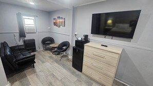 Un espace de vie compact comprenant un canapé, deux fauteuils, une petite table, un téléviseur, un four à micro-ondes et un meuble de rangement.