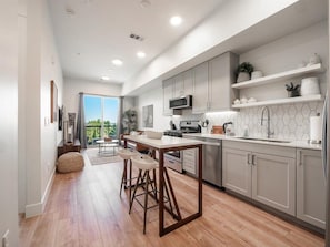 A modern kitchen with wooden flooring, a central island with stools, grey cabinets, and a view to the outside. - Fully furnished luxury top floor condo across from Regis University (Denver)
