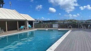 Ein Pool mit Liegestühlen und einer überdachten Liegefläche, umgeben von einer Holzterrasse und einem Zaun.