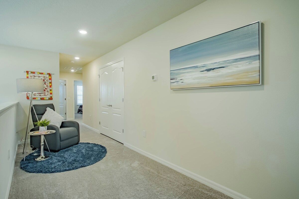 A hallway with a gray armchair, a small round table with a plant, and a blue rug.