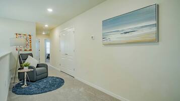 A hallway with a gray armchair, a small round table with a plant, and a blue rug.