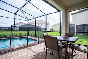 An outdoor patio with a pool, a table, and chairs.