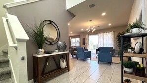 A spacious living area with a staircase, a console table with decorative items, and a seating area with two armchairs.