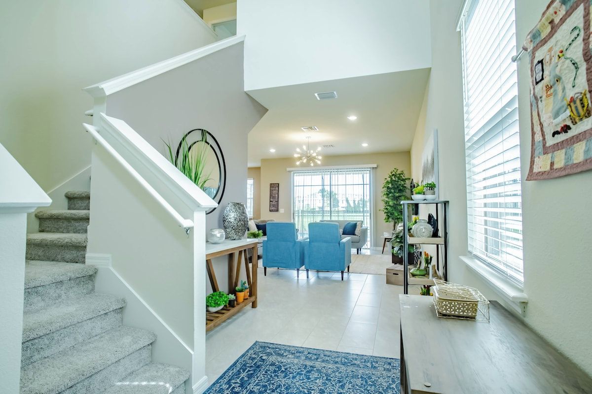 A modern interior with a staircase, a living area with blue chairs, and a dining table.