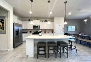 A modern kitchen with a central island, stainless steel appliances, pendant lighting, and a dining area with a bench.