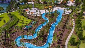 An aerial view of a resort with a winding pool, surrounded by palm trees and a golf course.