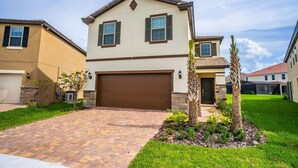 A two-story house with a brown garage door, a stone foundation, and a well-maintained lawn with a palm tree.