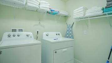 A laundry room with two washing machines, a drying rack, and shelves with folded towels.