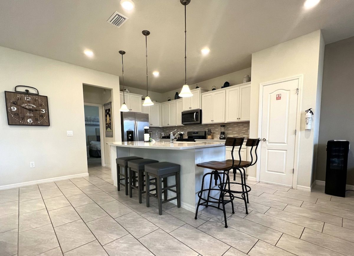 A kitchen with a central island, bar stools, a microwave, and pendant lighting.