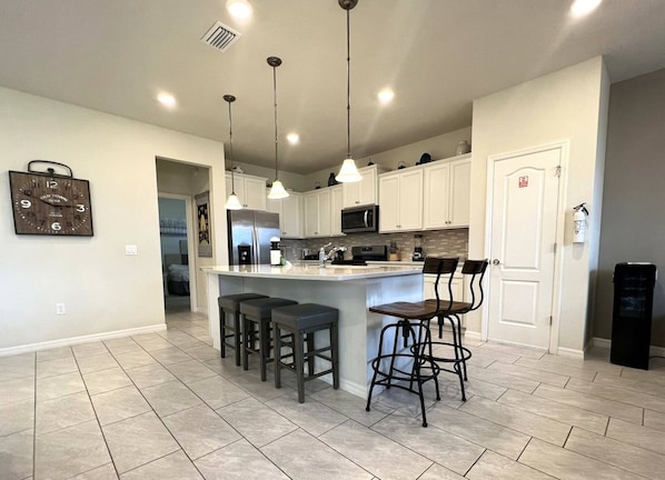 A kitchen with a central island, bar stools, a microwave, and pendant lighting.