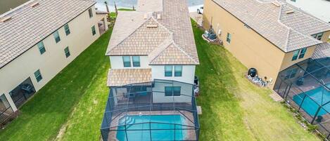 A residential area with a house featuring a swimming pool, surrounded by well-maintained lawns and neighboring houses.