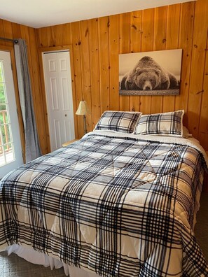 A bedroom with a plaid bedspread, a wooden paneled wall, a door, and a framed picture of a bear. - Hermitage Club and Mt Snow (Wilmington)
