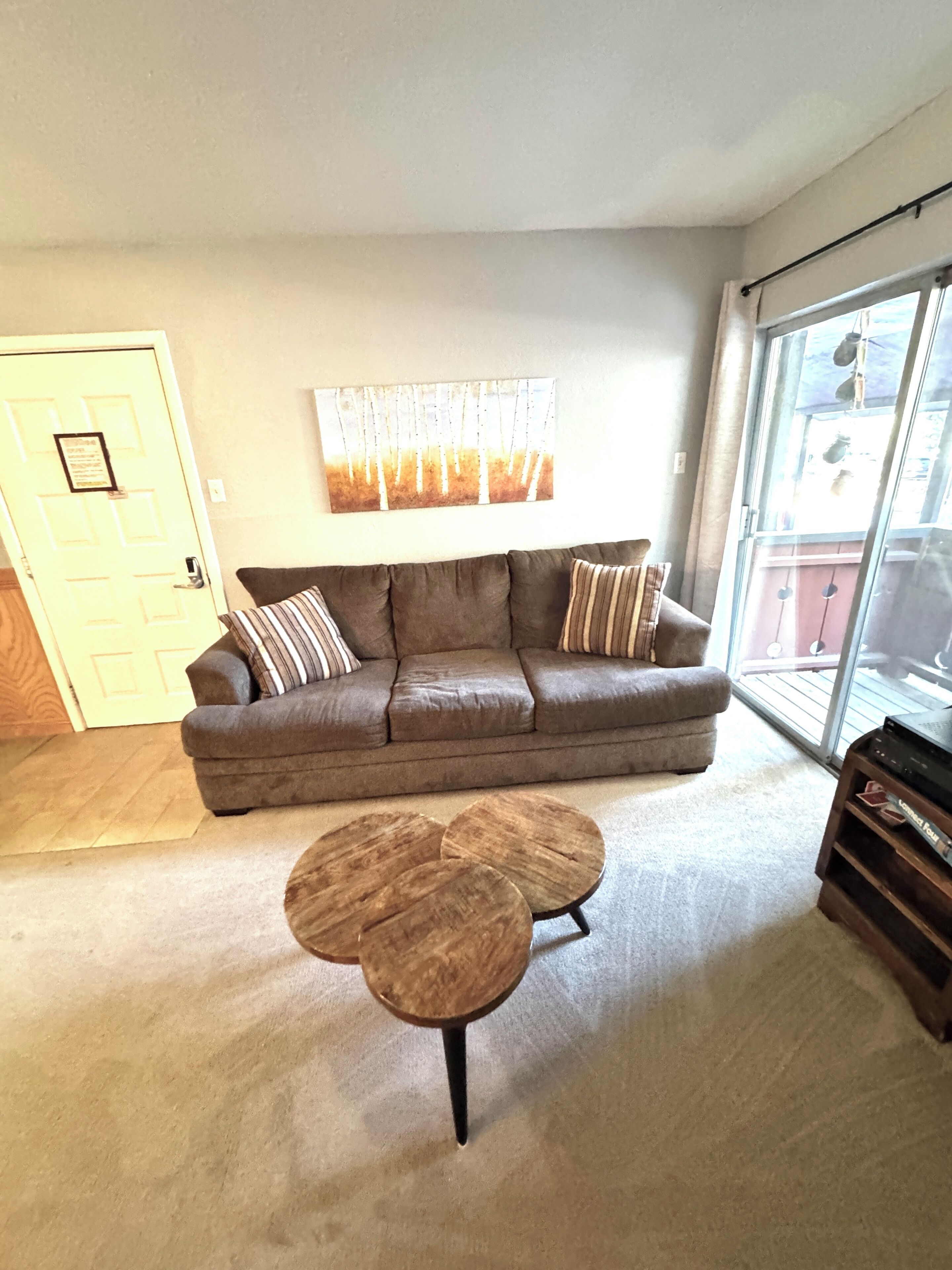 A living room with a brown leather sofa, two round wooden coffee tables, and a large window with a view of a balcony.